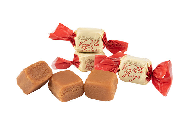 Traditional vanilla fudge candies presented with both wrapped and unwrapped pieces. The candies are packaged in cream-and-red twist wrappers, while the exposed fudge cubes showcase their soft texture, rich color, and handcrafted confectionery appearance.